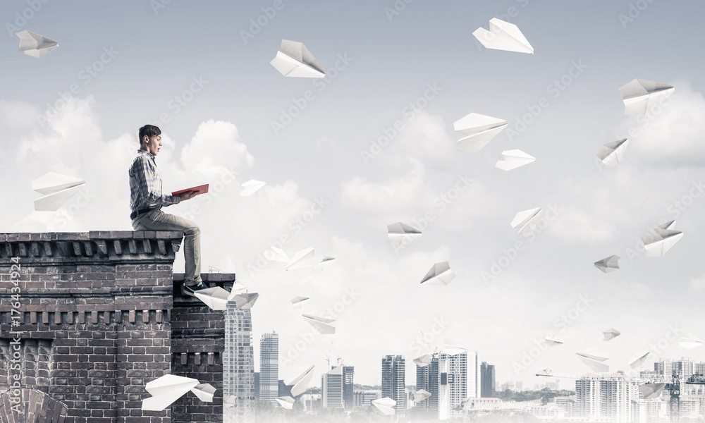 Handsome student guy on roof edge reading book and paper planes Handsome student guy on roof edge reading book and paper planes