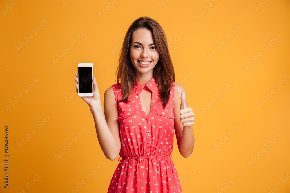 Naklejka premium Smiling brunette woman in dress showing blank smartphone screen
