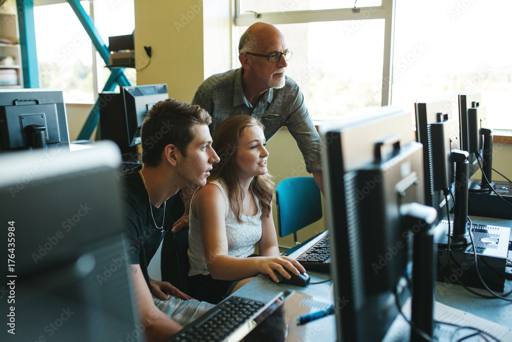 High school students working and learning with teacher in computer lab ...