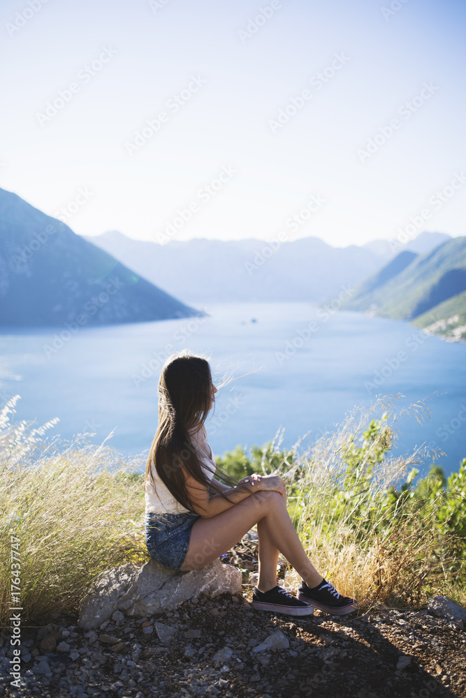 Young woman sitting on the rock by the peaceful sea at sunrise Young woman sitting on the rock by the peaceful sea at sunrise