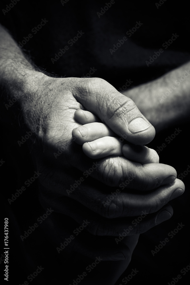 Hands of an elderly man holding the hand of a younger man.