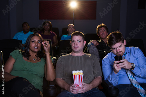 Annoyed guy trying to watch a movie being interrupted by rude people around him with no manners.