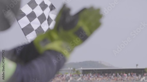 Man holding and waving Checkered race flag in slow motion at finish line on a raceway. Hands of unidentified person applauding.Victory, achievement, success and sport concept.