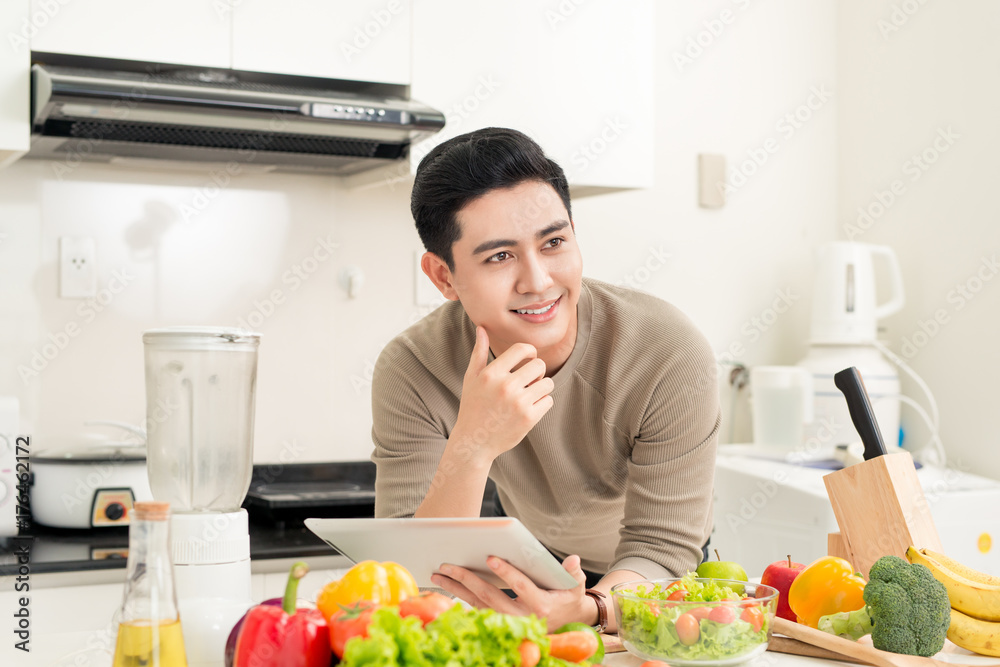 Asian handsome man looking recipe on laptop in kitchen at home Asian handsome man looking recipe on laptop in kitchen at home