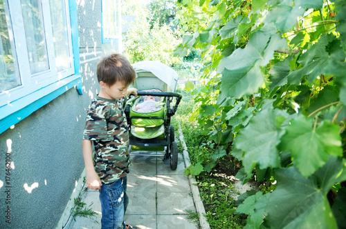 Fotografie Boy helping mother to snooze little baby in carriage outdoor