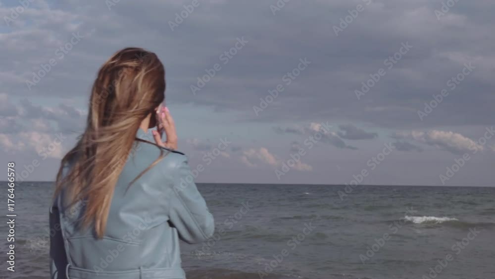 Young beautiful woman happily speaks by phone on the seashore Young beautiful woman happily speaks by phone on the seashore