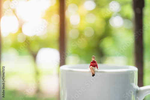 Miniature people, woman sitting on white cup on green nature background