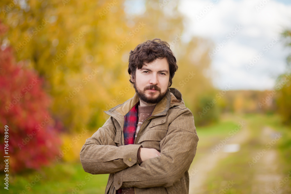 Portrait of young handsome bearded guy in the autumn city park.