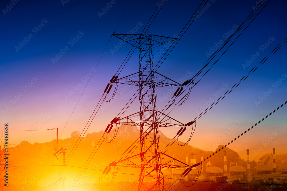 high voltage electricity transmission pylon silhouette with power plant against blue dusk sky
