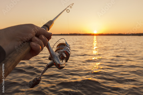 fishing rod in hand on sunset background photo