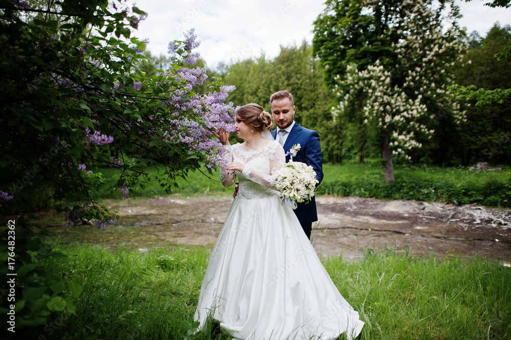 Stunning wedding couple enjoying each other's company in park with blossoming trees on the background. Stunning wedding couple enjoying each other's company in park with blossoming trees on the background.