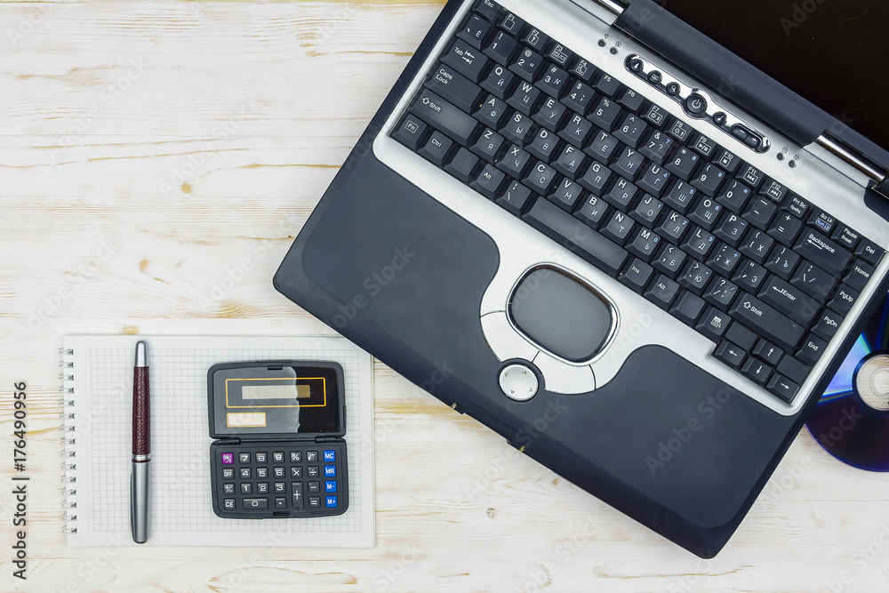 old laptop with a laser disk, calculator, notebook and pen on a wooden table
