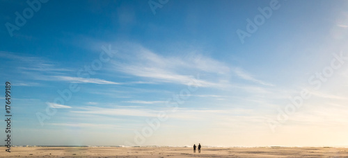 Couple wealking on an open, unpopulated beach. All alone.