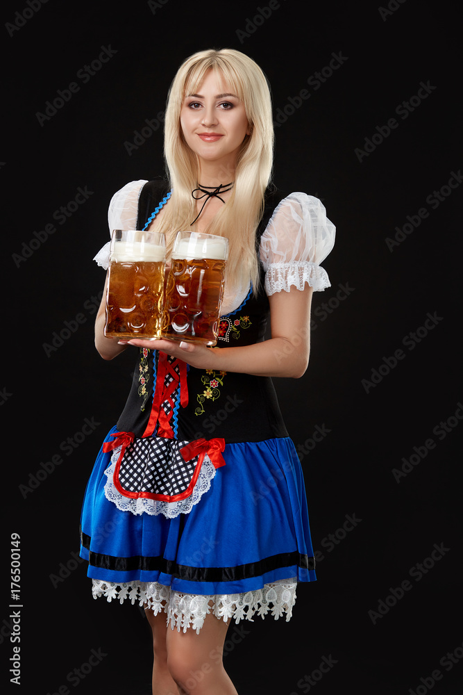 Young sexy woman wearing a dirndl with two beer mugs on black background. Young sexy woman wearing a dirndl with two beer mugs on black background.