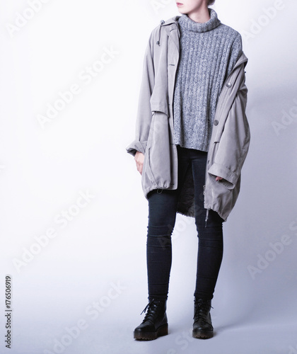 Woman wearing casual outfit with oversized parka jacket, grey knitted turtleneck sweater, black skinny jeans and black biker boots isolated on white background. Copy space. Fall or winter fashion 2017