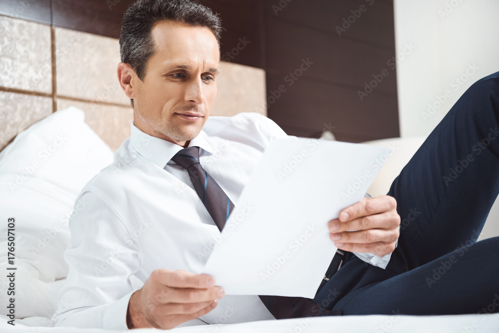 Businessman on bed reading paperwork