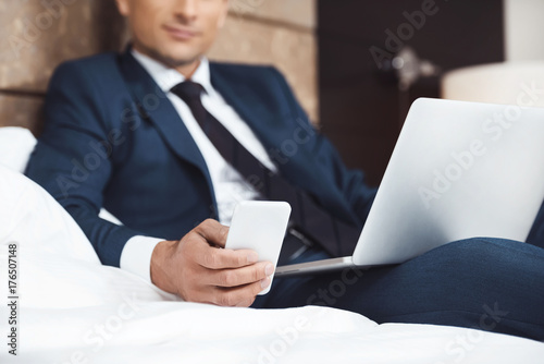 Businessman on bed with phone and laptop