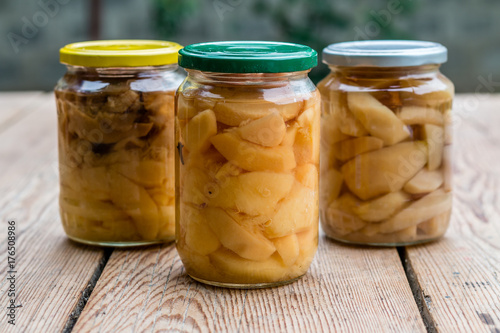 Canned apple and pear compotes, preserve in large glass jars outdoors on rustic wooden table