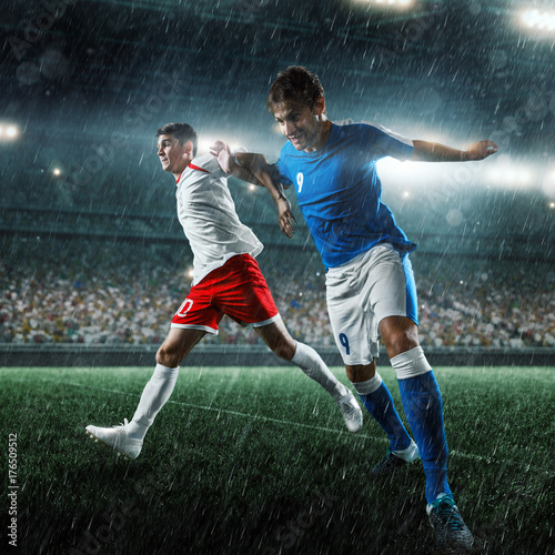 Soccer players performs an action play on a professional rainy stadium. Two football teams fighting for the ball. Players wears unbranded sport uniform. © Alex