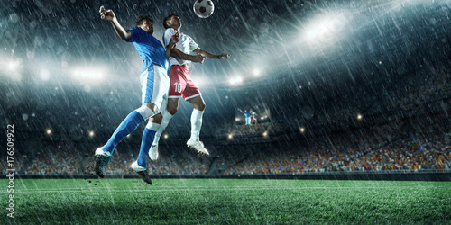 Soccer players performs an action play on a professional rainy stadium. Two football teams fighting for the ball. Players wears unbranded sport uniform.
