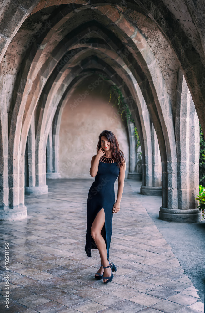 Fashion portrait of a young beautiful girl in black fashionable dress and black shoes on a neo-gothic terrace