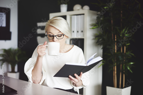 Woman reading book and drinking coffee at her desk photo