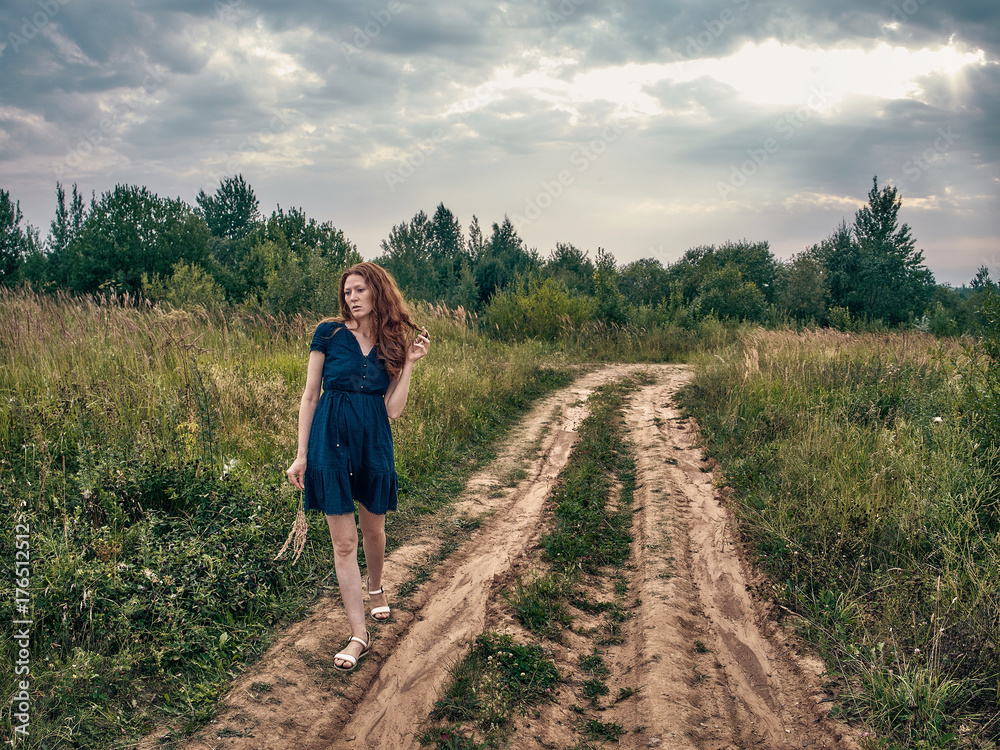 The red-haired girl in a blue summer dress strolls along the lake.