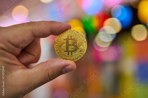 man's hand holding golden Bitcoin on Bitcoin mining background