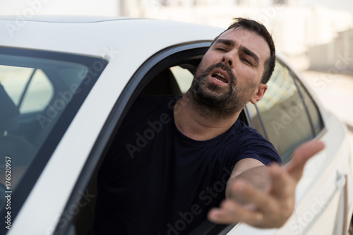 Angry driver pissed off by drivers in front of him and gesturing with hands. Road rage traffic jam concept.