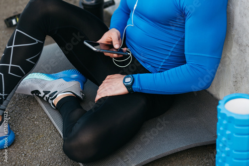 Young sports man in blue T-shirt siting on mat and listening music on the background of gray wall photo