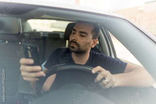 Man texting while driving.  Using a smartphone while driving.  Front view of man driving while using mobile phone.