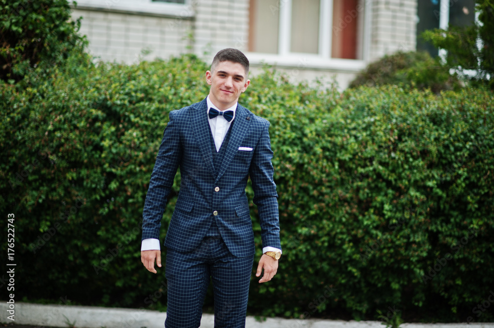 Portrait of a fashionable and stylish high school graduate in elegant tuxedo posing outdoor with bushes on the background. Portrait of a fashionable and stylish high school graduate in elegant tuxedo posing outdoor with bushes on the background.