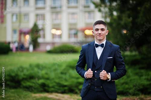 Portrait of a handsome young guy dressed in cool suit posing on the lawn on his prom day.