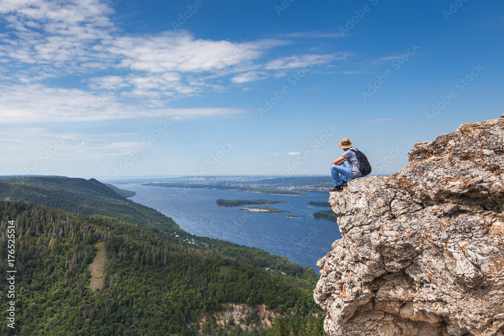 A man sits on a mountain and looks at a beautiful view