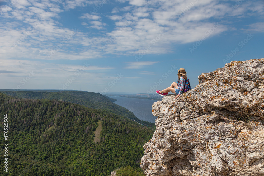 A young woman sits on a mountain and looks at a beautiful view
