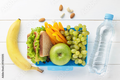 Blue lunch box with healthy food for school children with bottle of water on white wooden background.