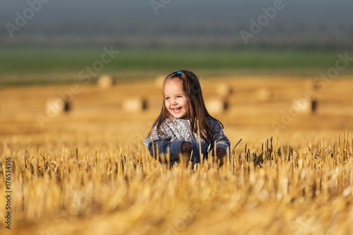 Happy 2 year old girl walking in a summer harvested field