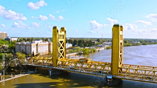 Cinematic aerial of Tower bridge in Sacramento downtown, capital of California state from waterfront view with docked boats, highway traffic and railroad trains on a hot sunny summer day 