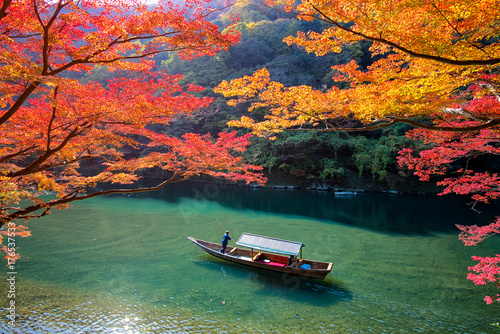 Boatman punting the boat for tourists to enjoy the autumn view along the bank of Hozu river in Arashiyama Kyoto, Japan.