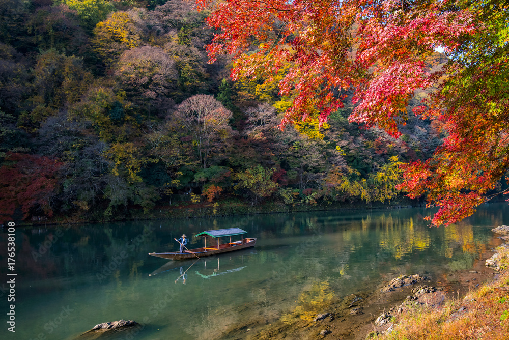 Fototapeta premium Boatman pływa łodzią dla turystów, aby podziwiać jesienny widok wzdłuż brzegu rzeki Hozu w Arashiyama Kioto w Japonii.