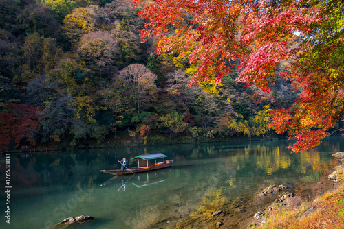 Boatman punting the boat for tourists to enjoy the autumn view along the bank of Hozu river in Arashiyama Kyoto, Japan. photo