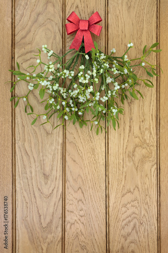 Christmas mistletoe bunch with red bow on oak wood background.