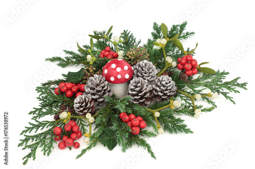 Fantasy winter and christmas table decoration with fly agaric mushroom ornament, holly, ivy, mistletoe, ivy, juniper and cedar cypress leaf sprigs and pine cones on white background.