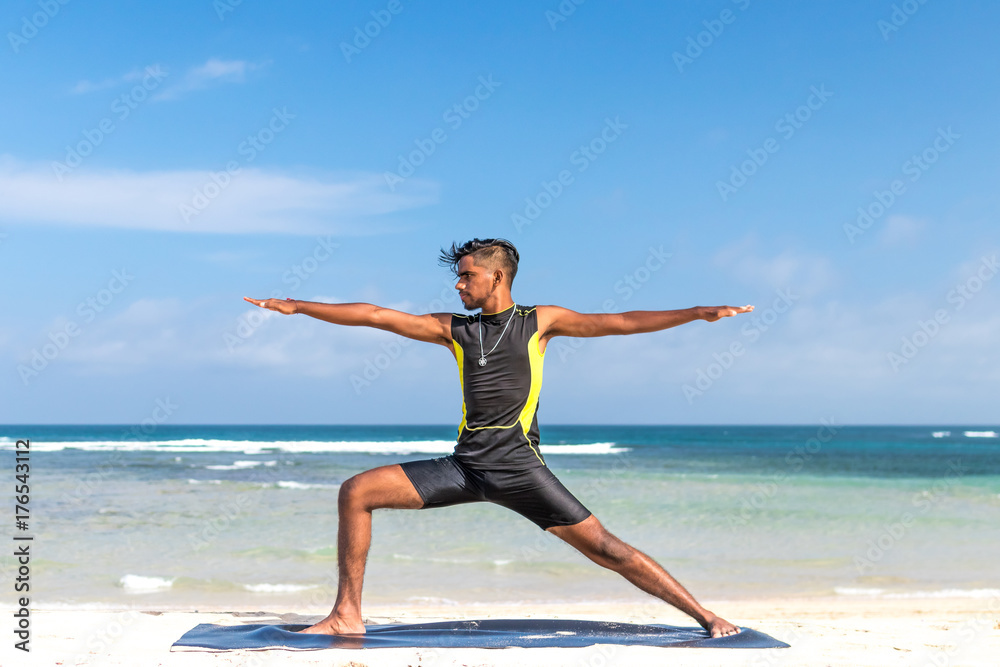 Asian yoga man practice yoga on the beach with a clear blue sky background. Yogi on the tropical beach of Bali island, Indonesia.