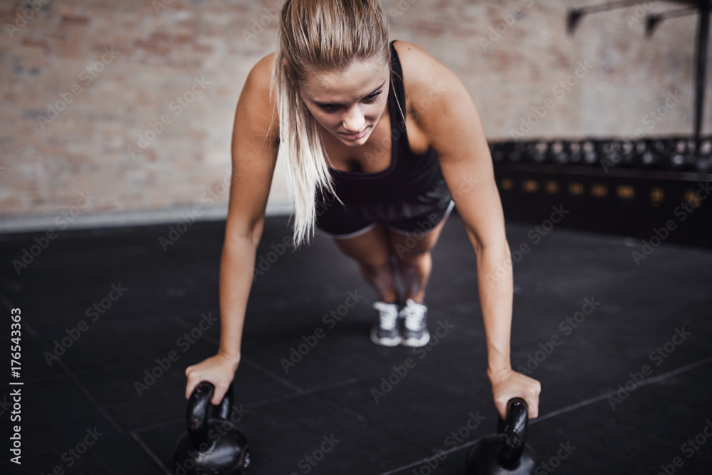 Focused young woman doing pushups with weights in a gym