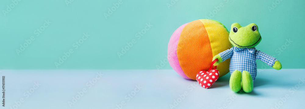 Kids Toys Small Frog Holding Red Heart Multicolored Textile Soft Ball on Blue Green Background. Banner Charity Nursery Hospital Childhood Copy Space