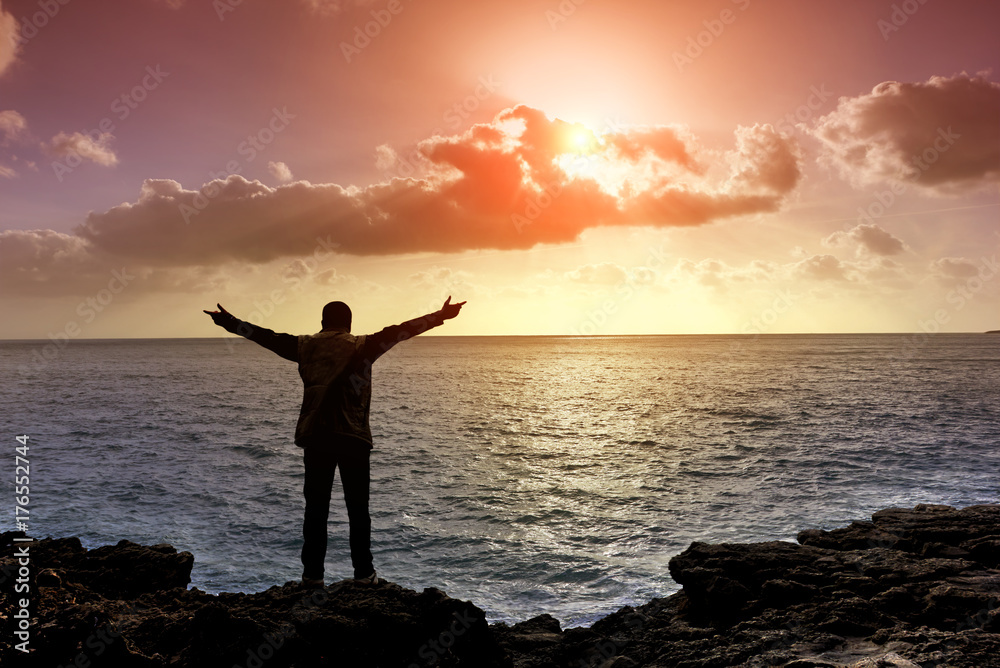 Fototapeta premium Man with arms outstretched on cliffs, Cloudy sunset at seascape