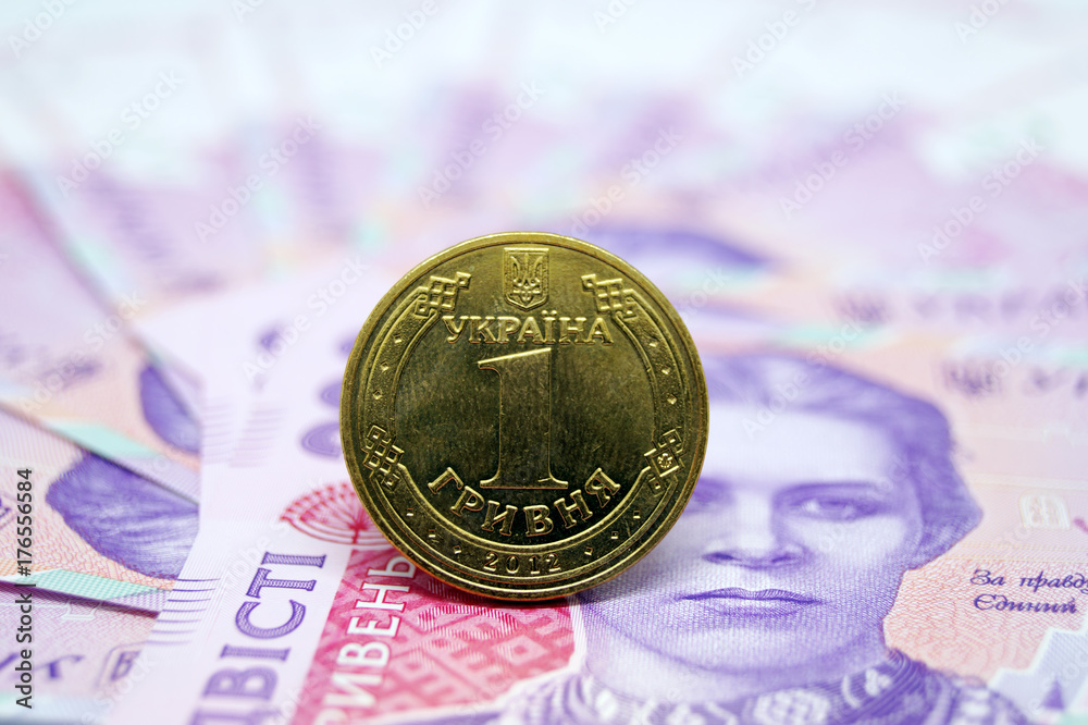 The coin is one hryvnia against the background of paper banknotes of the Ukrainian currency.