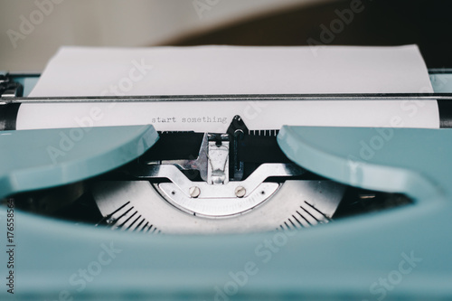 retro blue typewriter with the message start something typed on the paper
