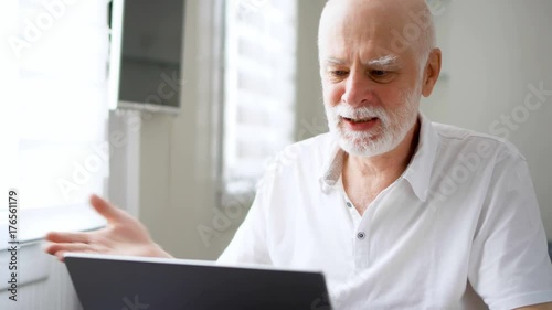 Handsome elderly senior man receiving very bad news on his laptop computer screen, upset and frustrated with failure, troubled by financial difficulties. Active life after retirement concept.